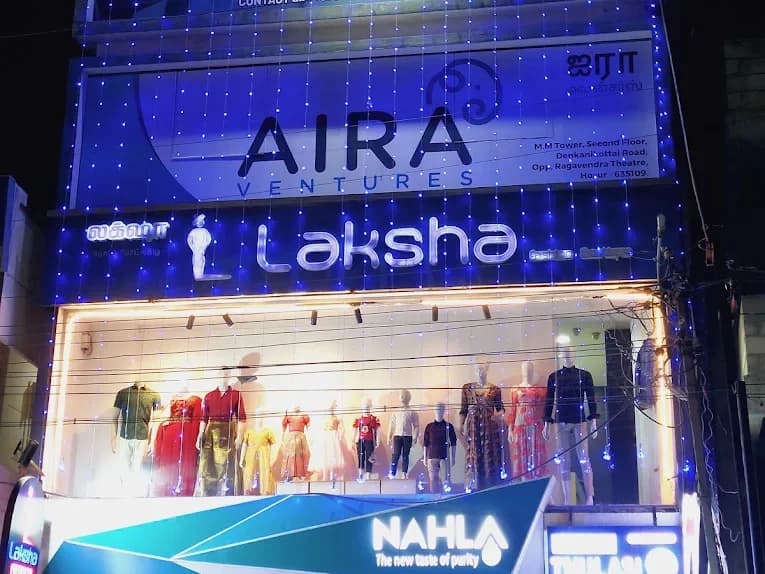 MM Tower at night, lit up, with the illuminated Laksha sign above a window of mannequins in women's, men's and kids' clothing